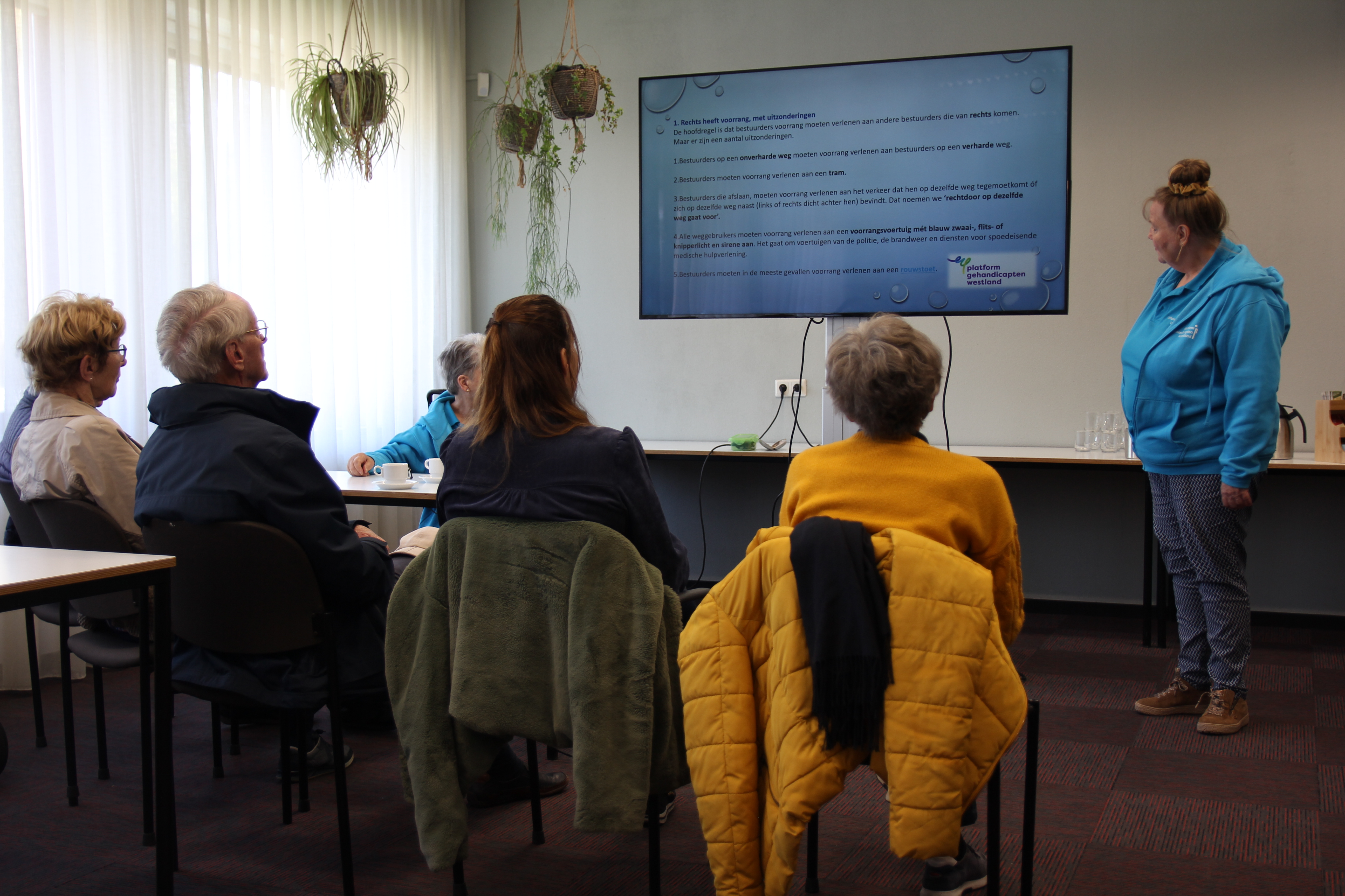 Een groepje mensen kijkt toe hoe een vrijwilligster uitleg geeft op een digibord.